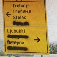 A road sign in Bosnia with the cyrillic text intentionally blacked out by graffiti